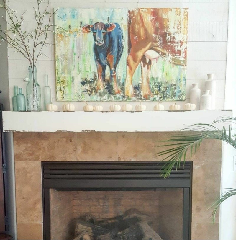 fireplace with cow painting and white pumpkins
