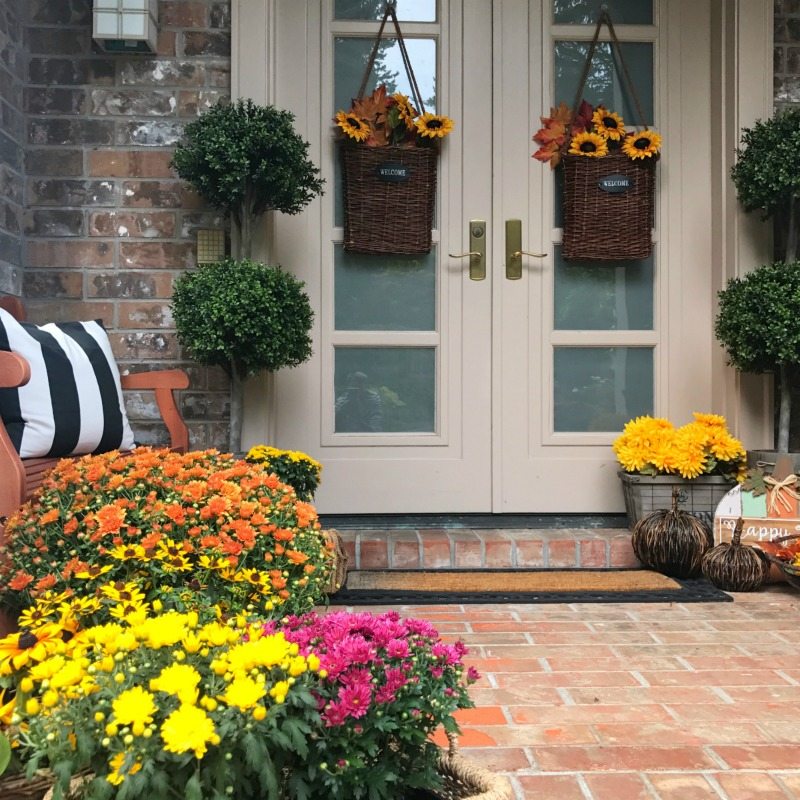 fall front door decorated with mums baskets of flowers and pillows