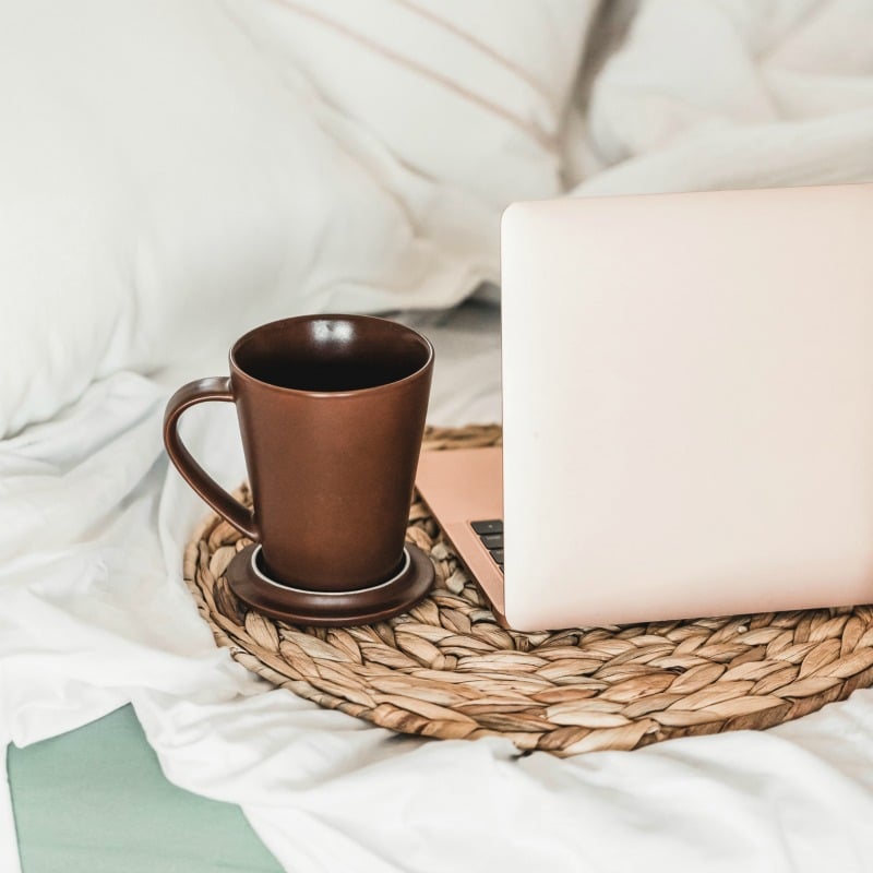 IG trust score, Rose colored laptop on bed with woven placemat and brown coffee cup.