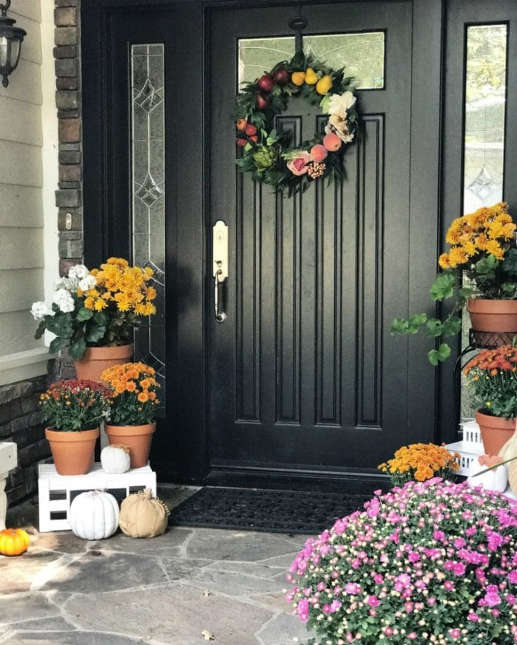 Black front door with fall wreath and fall mums and pumpkins