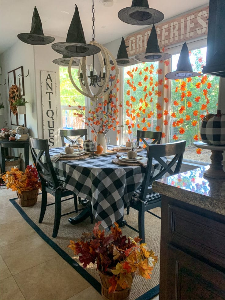 Festive Halloween table decorated with floating witch hats, autumn leaf garlands and buffalo plaid.