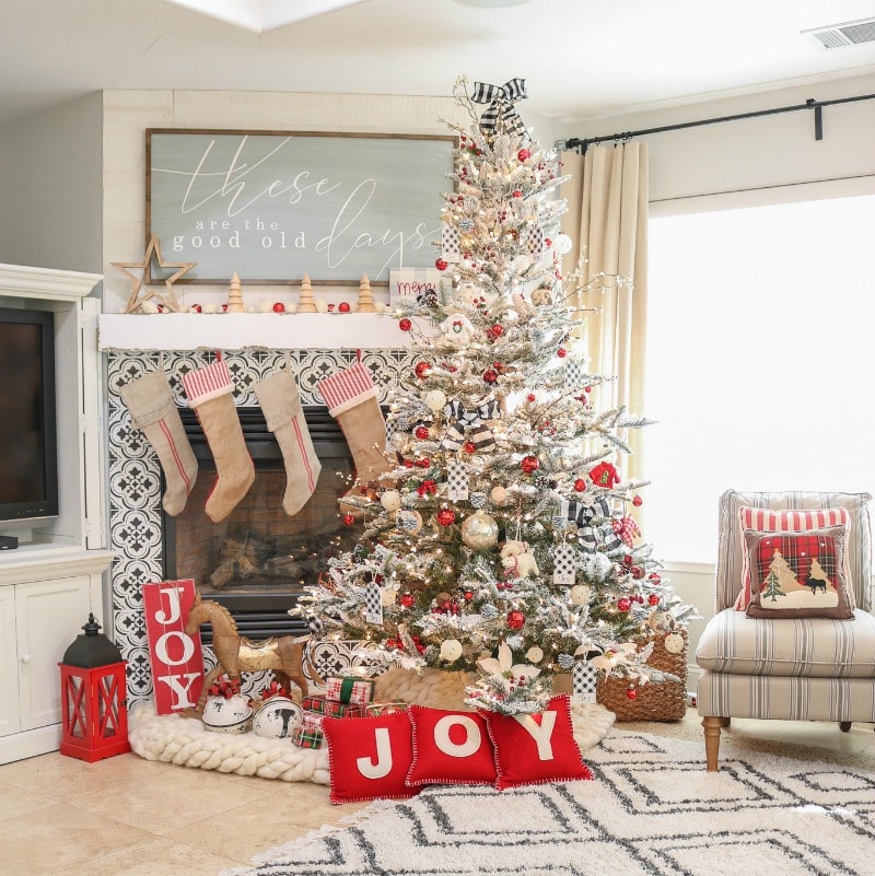 Beautiful flocked decorated realistic artificial Christmas trees with red and black decorations by the fireplace hung with burlap stockings