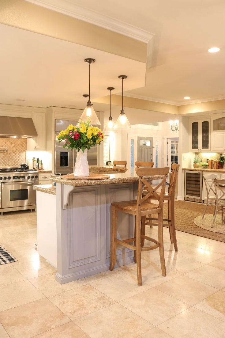 white painted kitchen cabinets in large great room with hanging pendent light lights and shiny stone floor