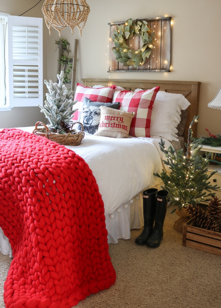 guest bedroom decorated for christmas with red chunky knit throw and mini christmas trees