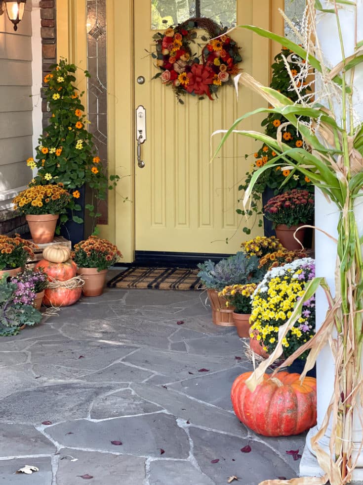 gold painted front door with front porch decorated for fall with pumpkins and mums