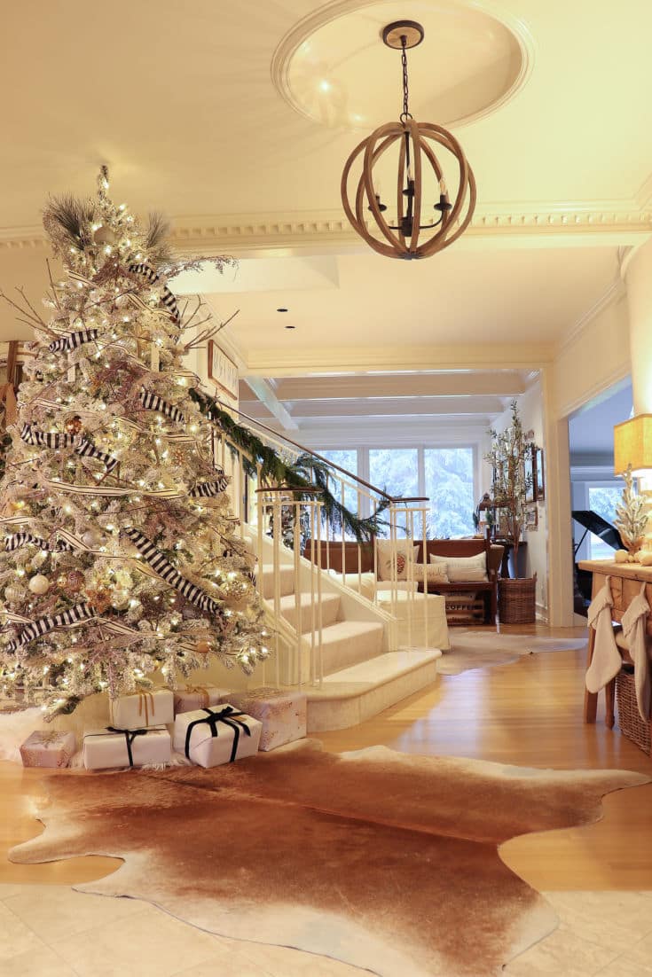 Artificial flocked tree is elegant in beautiful foyer next to staircase