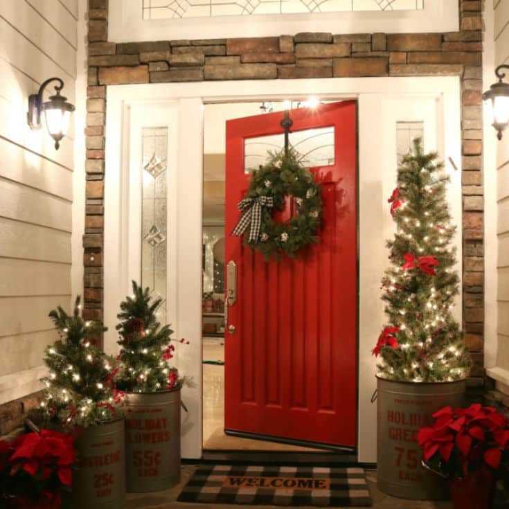 Front porch decor for Christmas is easy with red door and lots of twinkle lights and mini Christmas trees