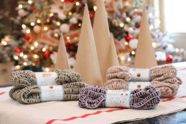 mambo yarn in three colors and cardboard cones in three sizes in front of Christmas tree