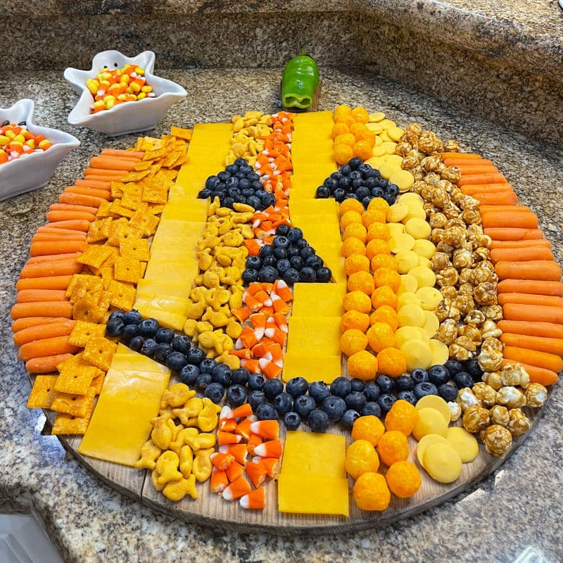 orange foods on a board shaped to look like a Halloween pumpkin