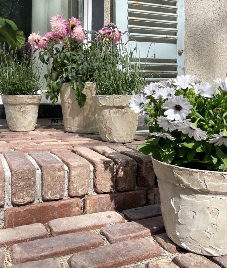 Faux stone planters with flowers on brick step