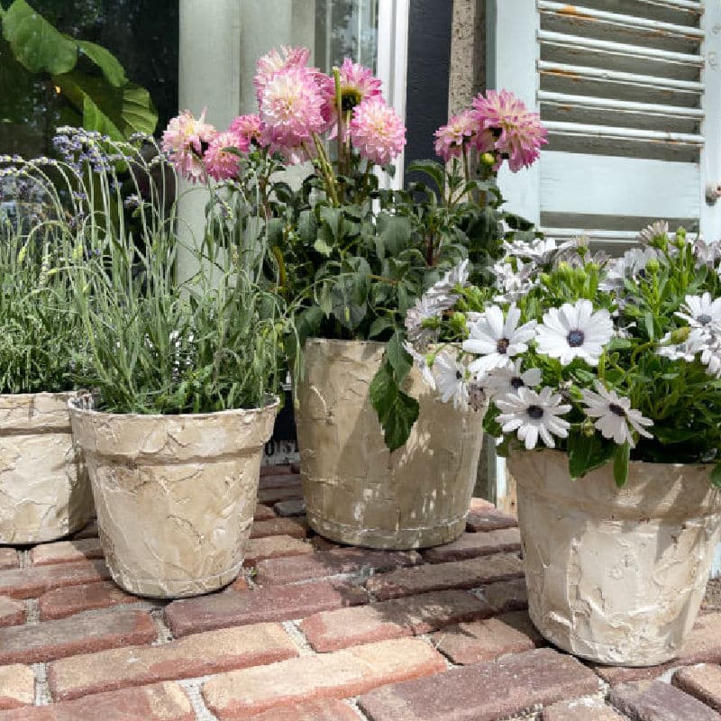 faux stone planters with flowers on a brick porch