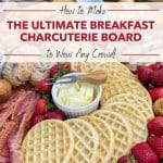 Big board featuring a charcuterie breakfast including waffles, strawberries, muffins, fruit, and bacon.