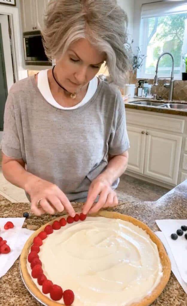arranging fruit on a sugar cookie pizza crust, topped with cream cheese icing