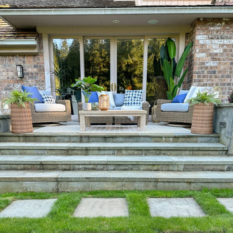 modern outdoor patio space featuring a beautiful outdoor rug, gray wicker rattan patio furniture, and warm decor elements.