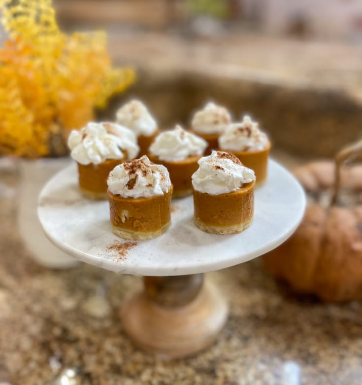 pumpkin pie shooters topped with whipped cream sit on top of a marble pedestal