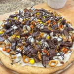 A close-up of a Dessert Pizza, showcasing a sugar cookie crust covered with a colorful array of leftover Halloween candy pieces and drizzled with milk chocolate.